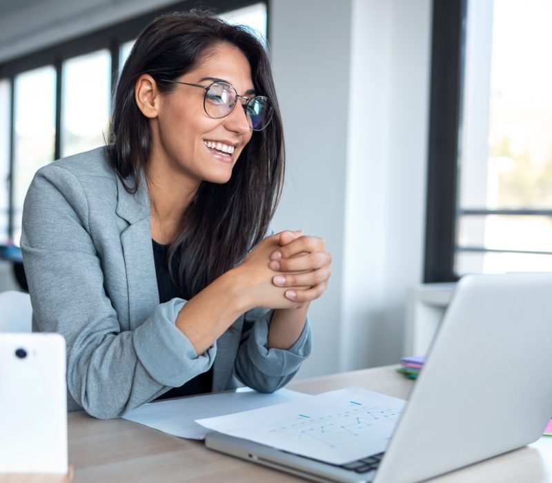 Shot of confident business woman looking and speaking through the webcam while making a video conference with laptop from the office.